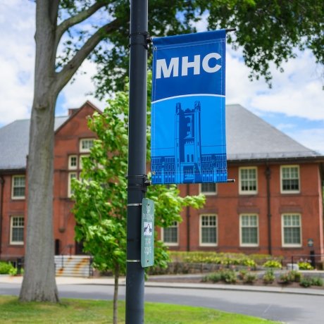 Mount Holyoke campus - a banner on a sign with MHC and the clock tower. Photo by Max Wilhelm, 2024.